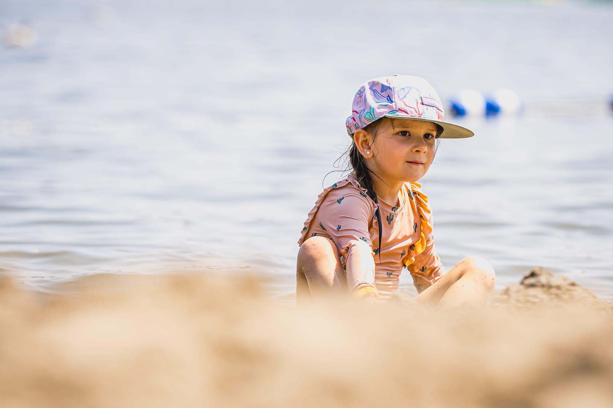 Une petite fille assise sur le sable sur le bord d'un lac
