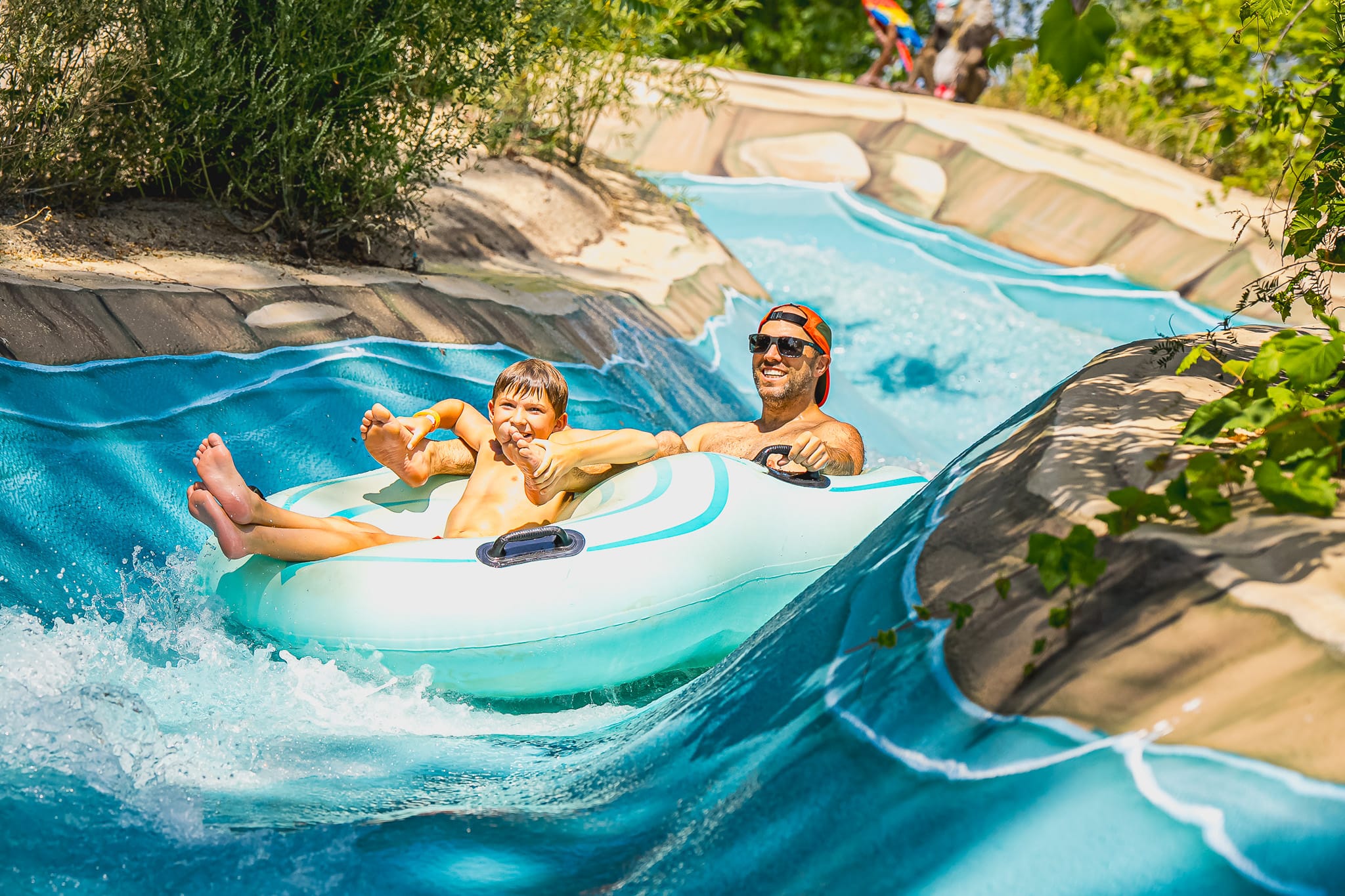 Un homme et son enfant qui glisse dans un tube à deux personnes