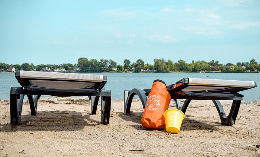 Chaises longues avec sac orange et sceau jaune sur plage et lac
