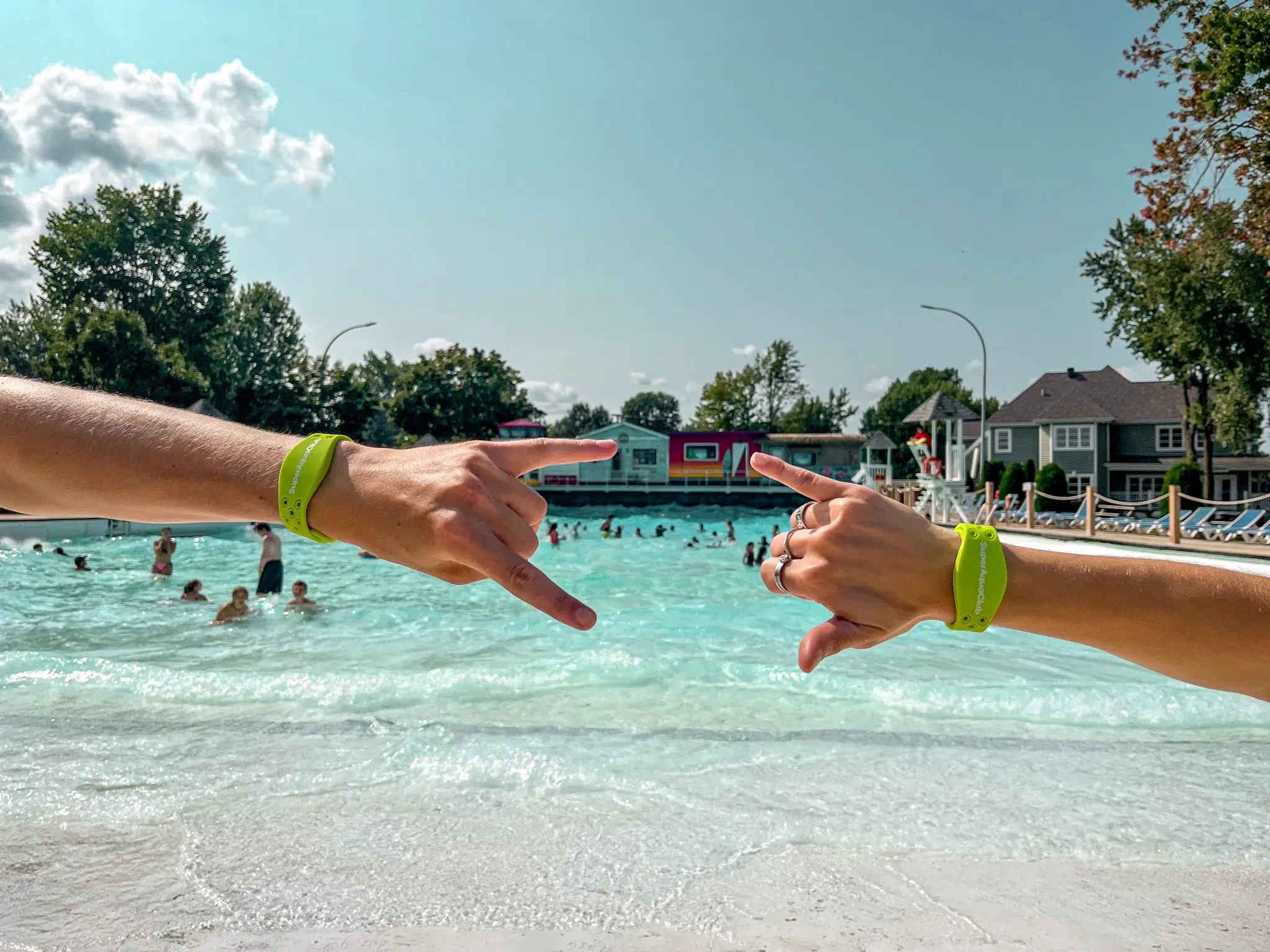 Deux bras portant un bracelet vert devant une piscine à vagues