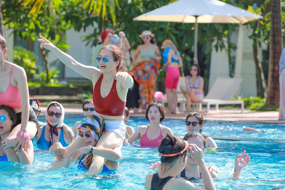 Men engage in playful acrobatic lifts and team-building fun in the swimming pool, showcasing strength and camaraderie during a recreational break.